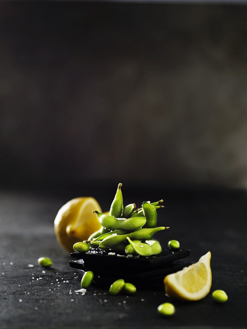 Raw soya beans with pods on a black slate platter with a sliced lemon