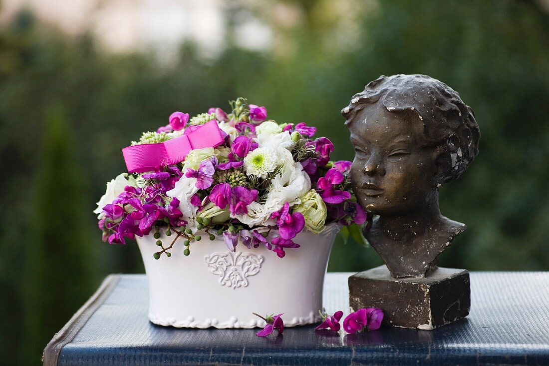 Romantic flower arrangements and bust of woman on top of vintage suitcase outdoors