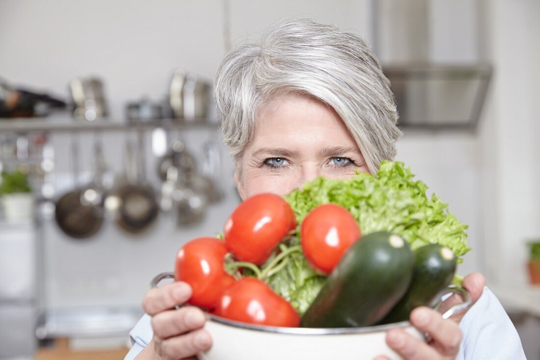 A middle-aged woman holding a colander of fresh vegetables
