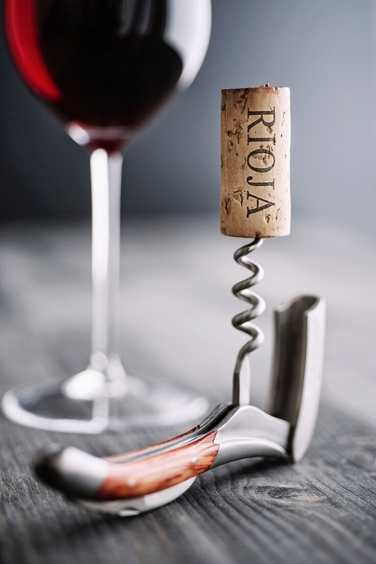 An arrangement featuring a glass of red wine, a corkscrew and a Rioja cork