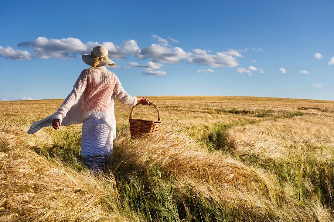 Woman wearing straw hat and carrying basket walking through summer cornfield