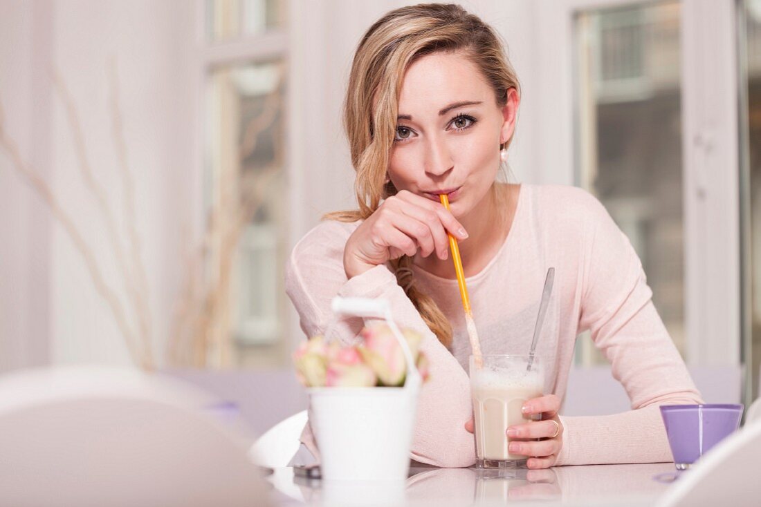 A young woman sitting at a table in a cafe drinking a latte macchiato with a straw