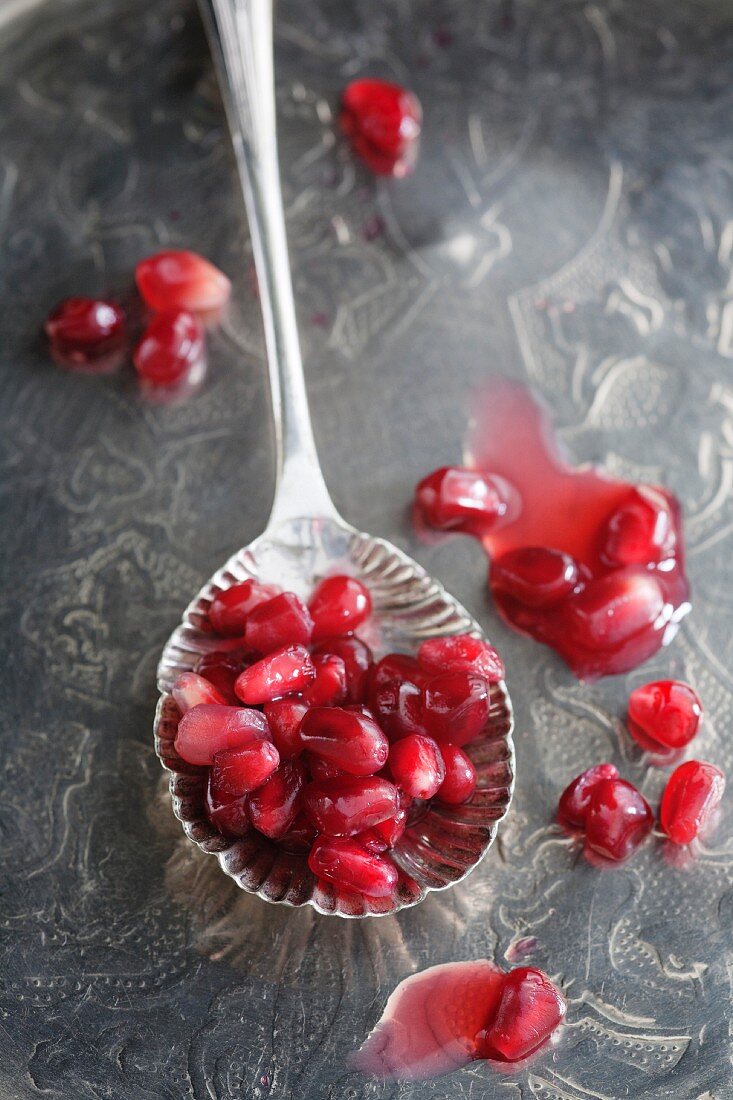 Pomegranate seeds on a spoon and a silver tray