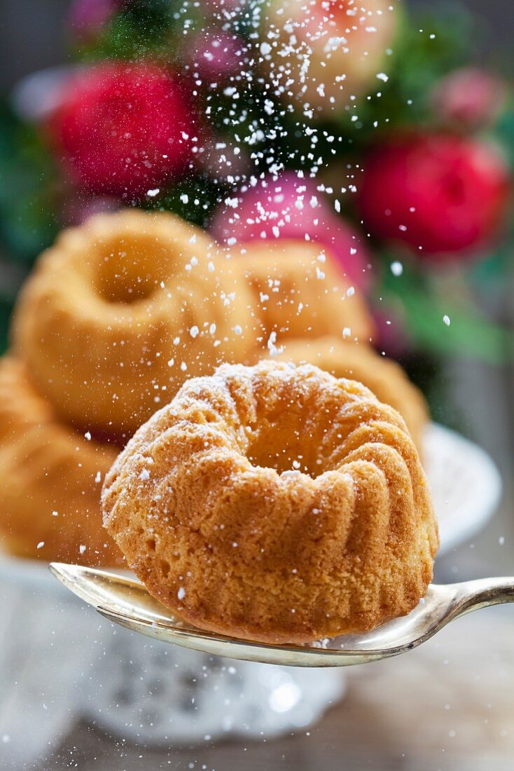 A mini Bundt cake on a spoon being dusted with icing sugar