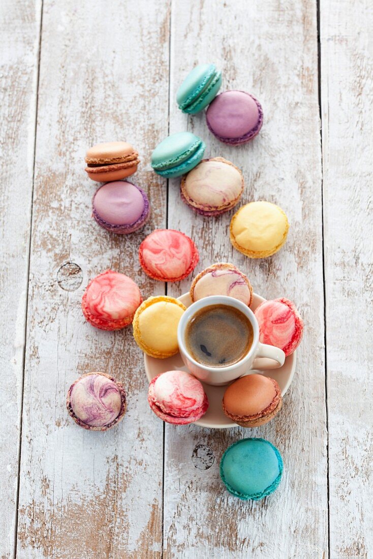 A cup of coffee surrounded by a variety of colourful macaroons