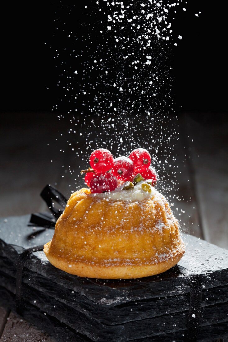 Icing sugar being dusted onto a mini Bundt cake with ricotta cream and redcurrants