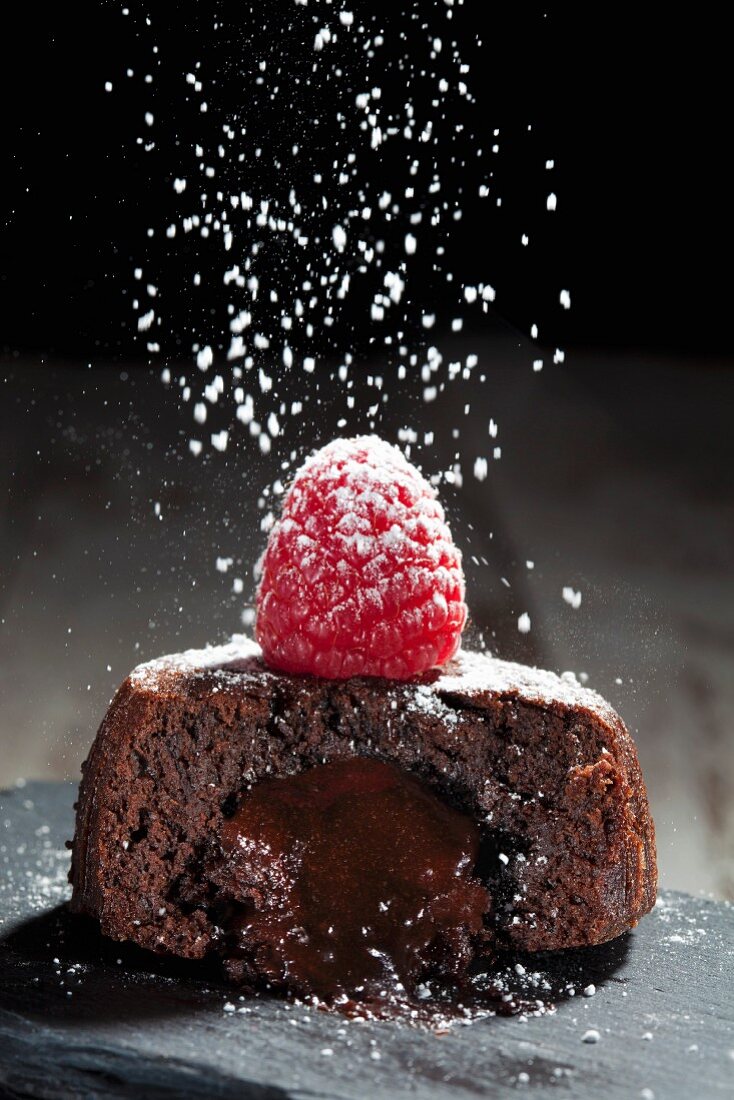 Icing sugar being dusted onto a chocolate cake with a liquid core