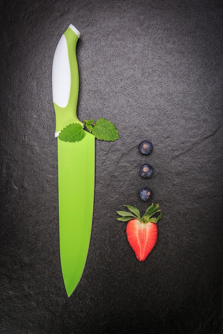 An arrangement featuring blueberries, a strawberry and green knife on a slate surface