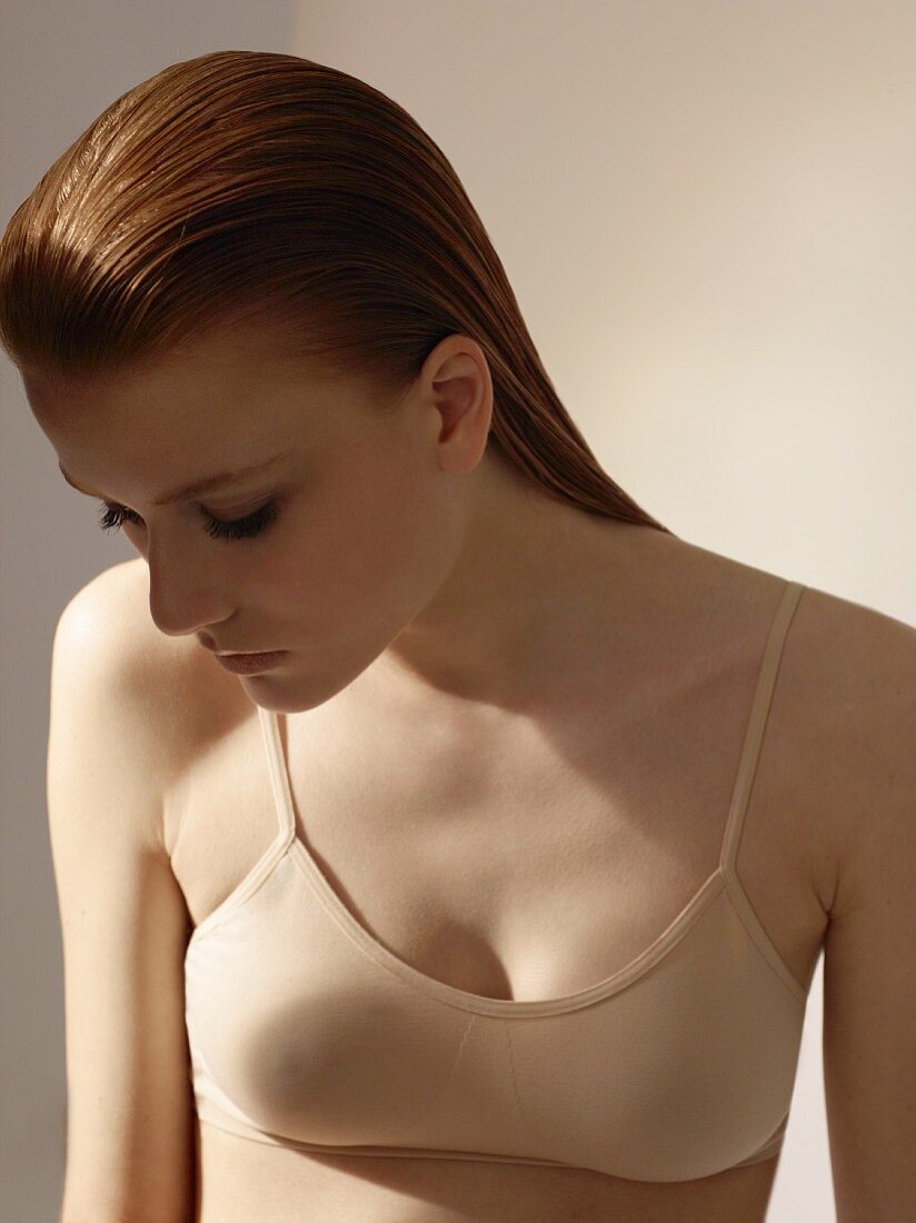 A young woman with damp red hair and a beige bra