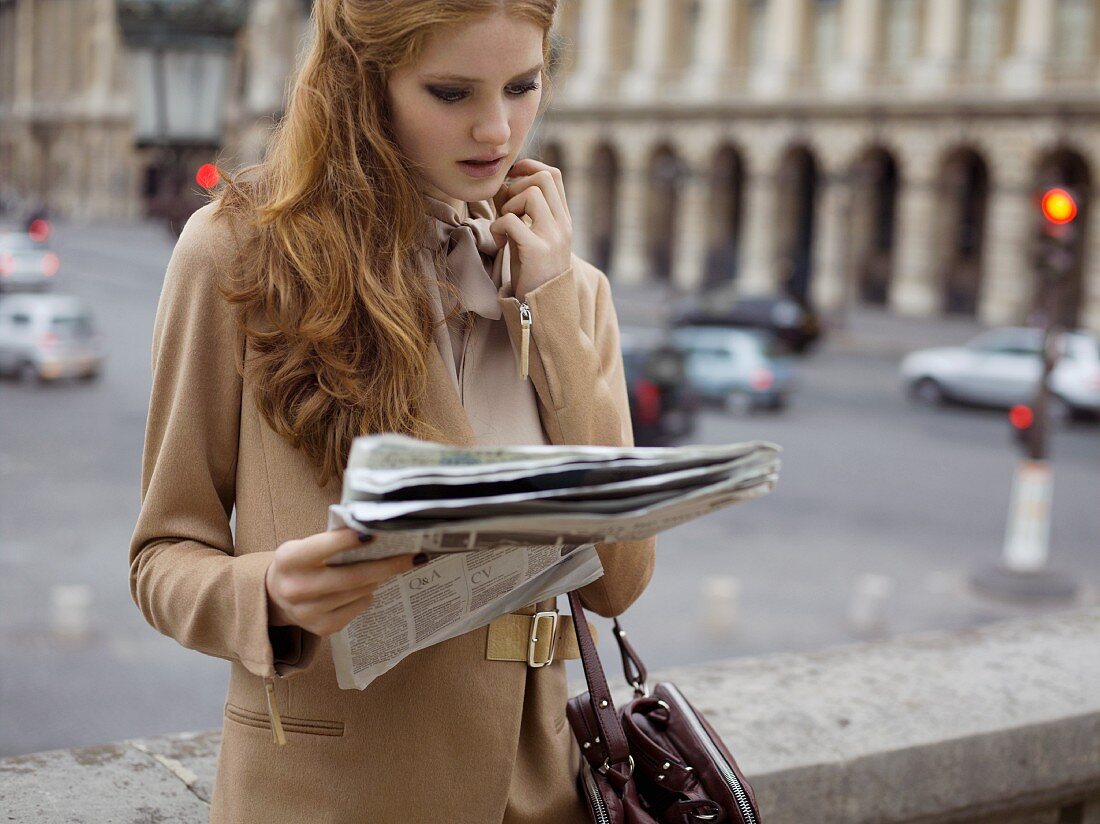 A young woman wearing a sand-coloured blazer reading a newspaper
