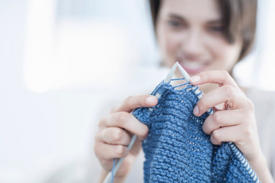 Woman knitting a blanket using blue yarn