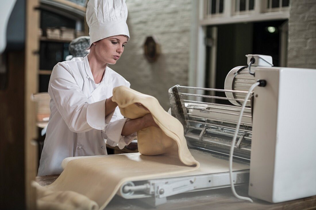 A baker using a machine to roll out dough in a bakery