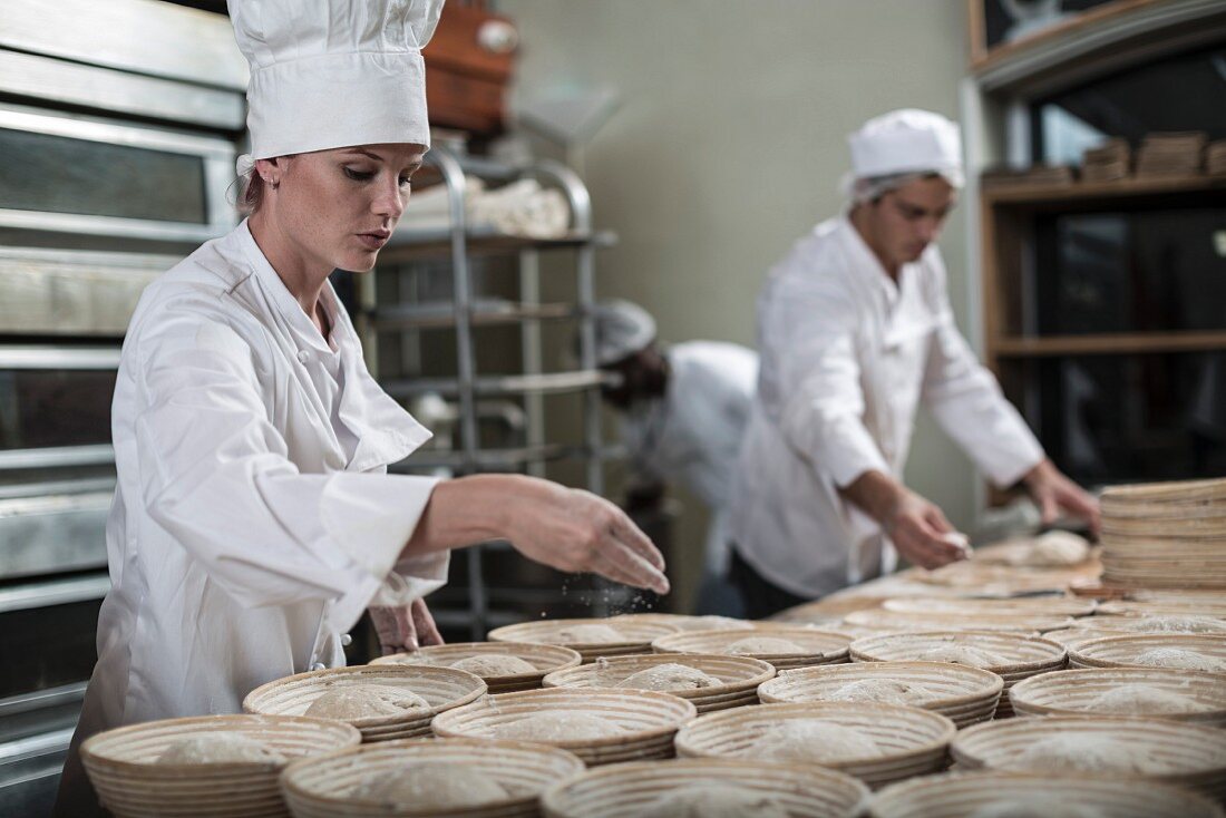 Bäcker bei der Brotherstellung: Brotteig in Backformen mit Mehl bestreuen