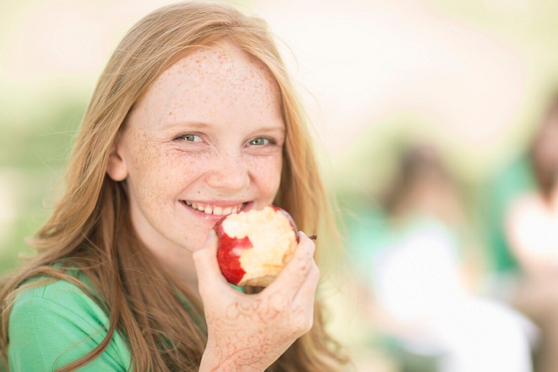 A teenager with red hair eating an apple