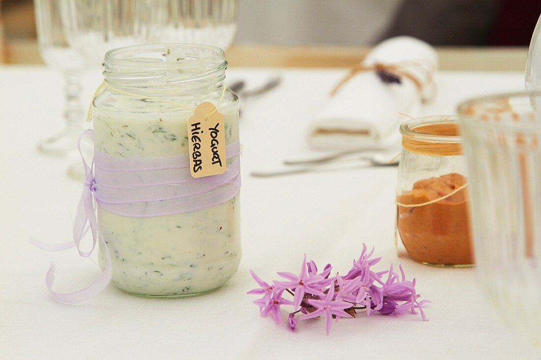 Kräuter-Joghurt in Glas mit lila Schleife auf Tisch