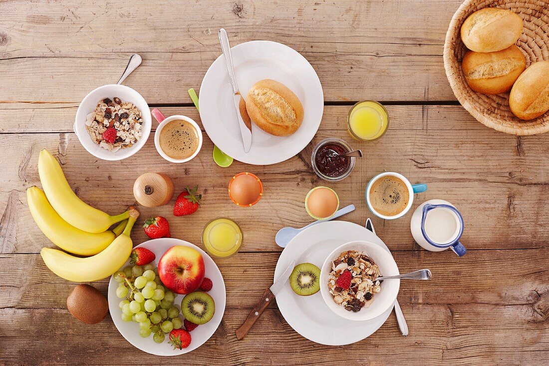 Frühstück mit Semmeln, Müsli, Obst, Eiern & Kaffee auf Holztisch (Aufsicht)