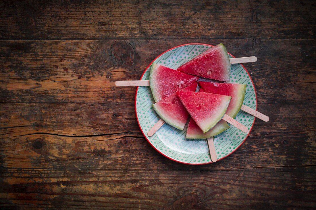 Watermelon ice cream sticks on a plate on a wooden surface (seen from above)