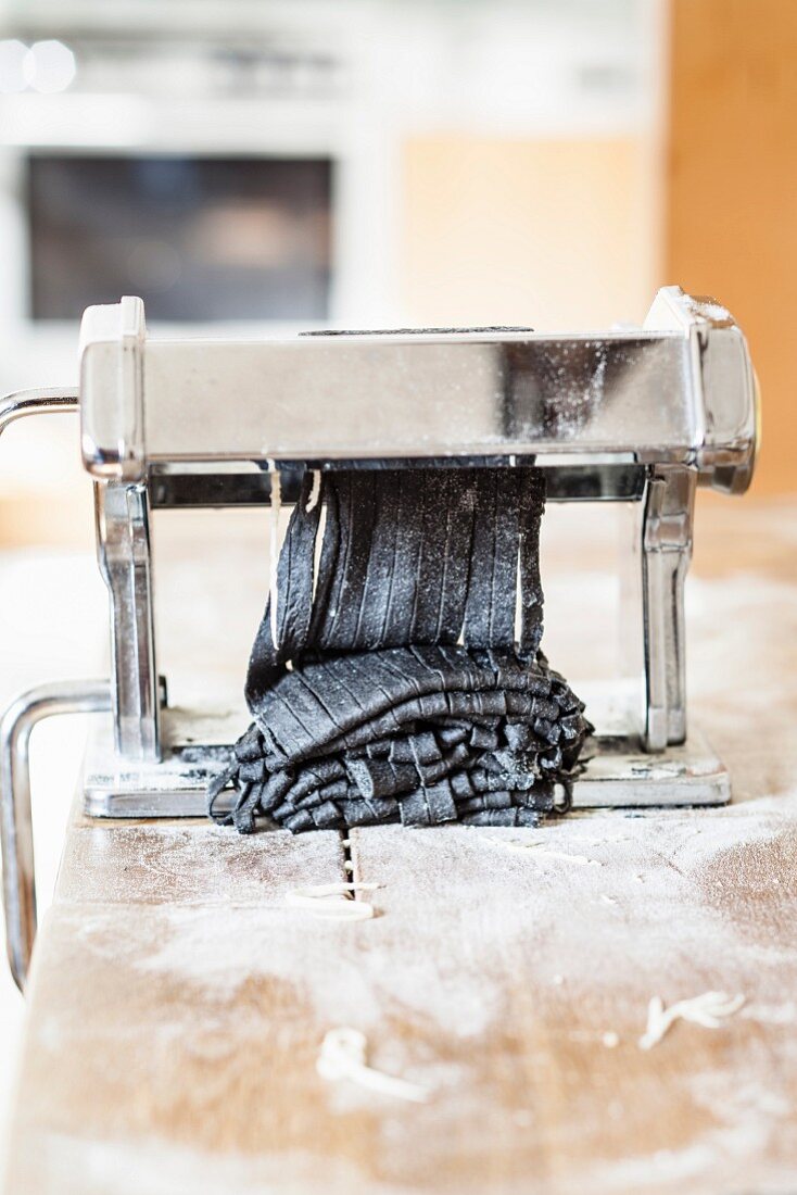 Black tagliatelle being made with a pasta machine
