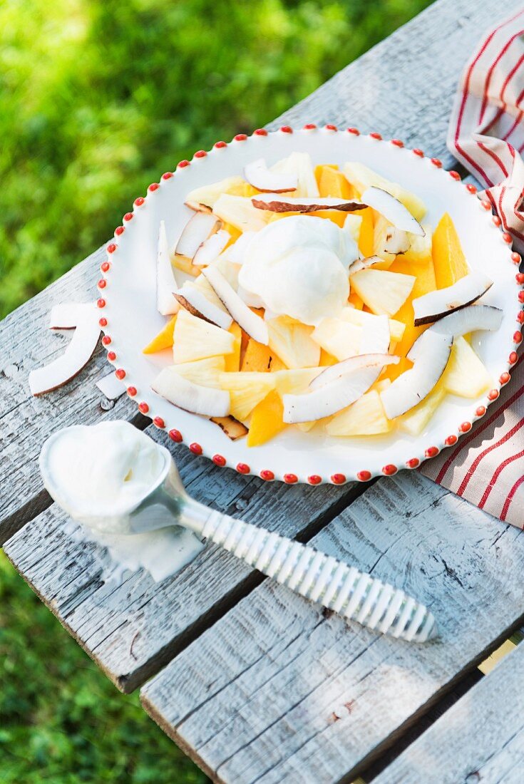 Yellow summer fruit salad with mango, ice cream and coconut