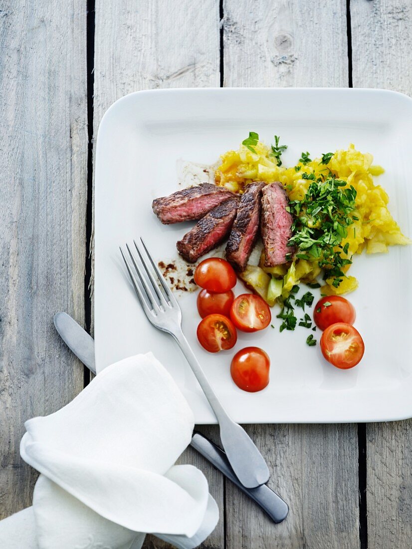 Beef steak with a herb potato salad, gherkins and tomatoes
