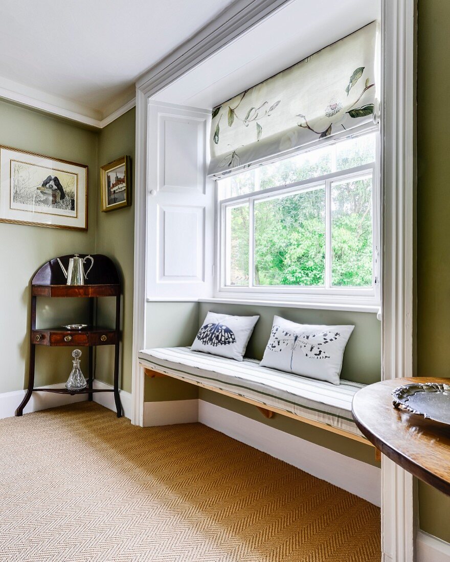 Window seat in large window niche next to antique quarter-round corner table