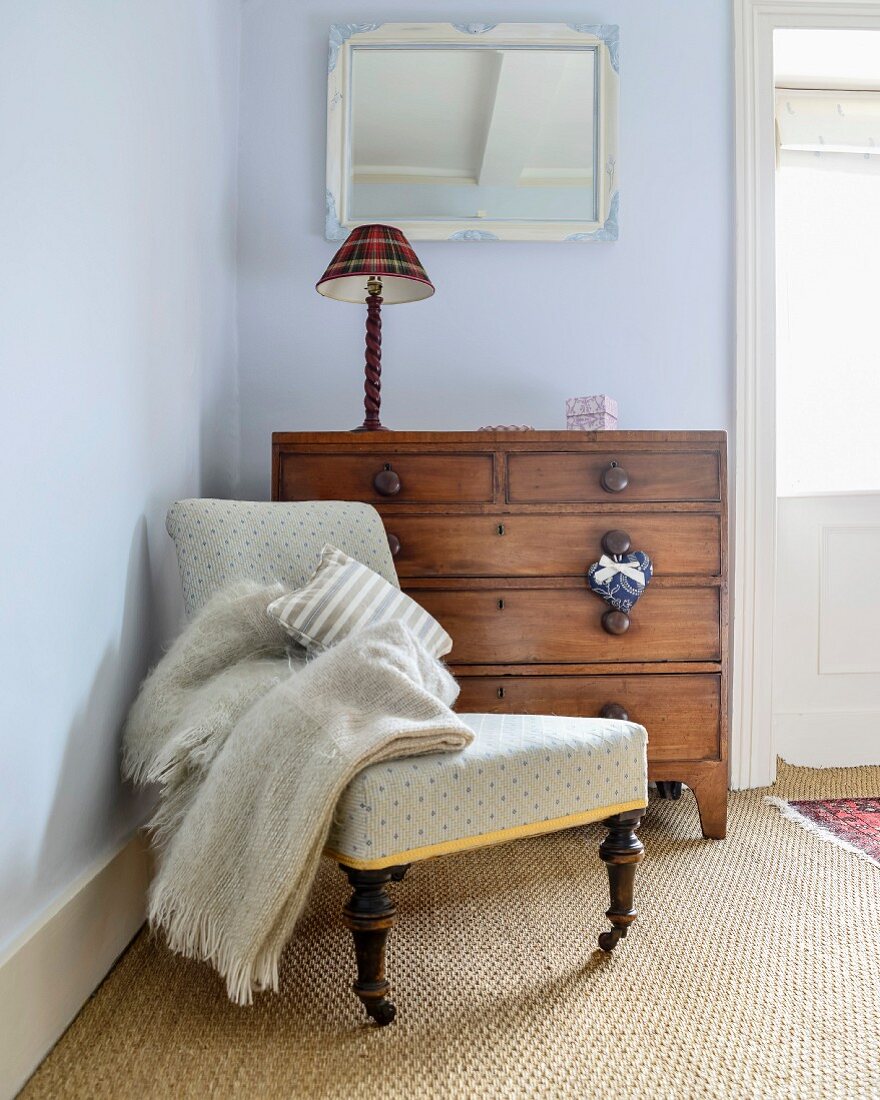 Antique easy chair and chest of drawers in corner of room painted pale blue