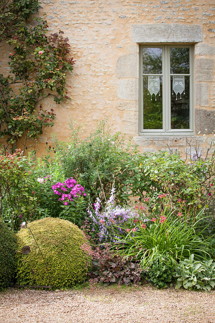 Clipped box balls and flowering plants in front of stone façade