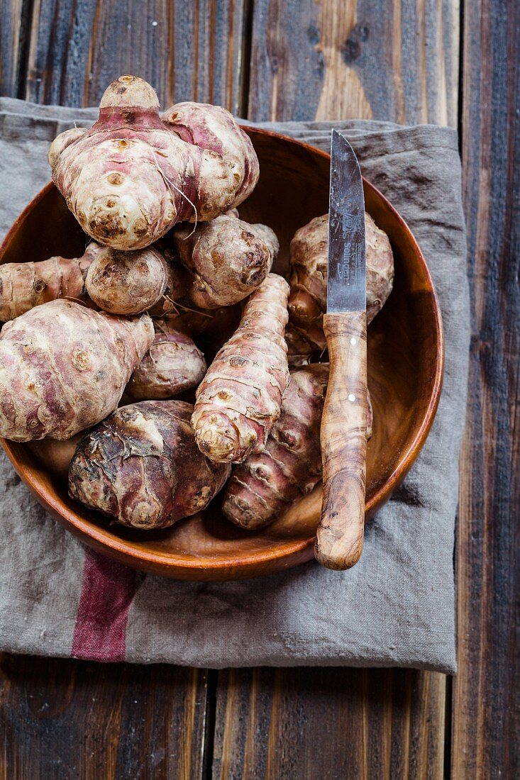 Jerusalem artichokes in a wooden bowl with a knife