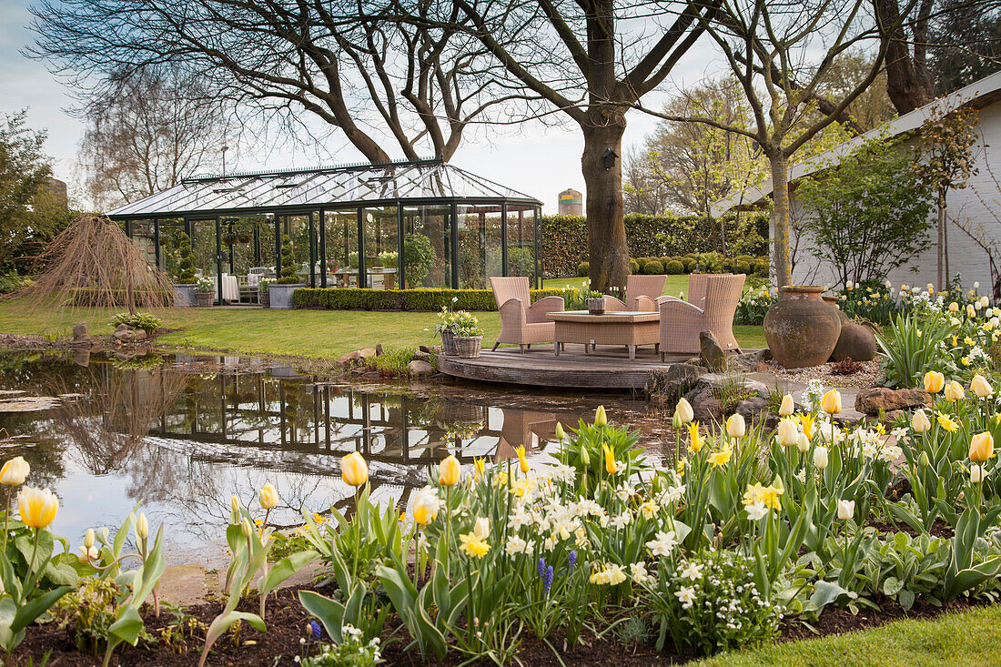 Garten im Frühling mit Teich, Sitzplatz und Glashaus