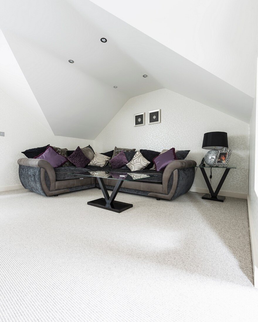 Corner sofa under sloping ceiling with recessed spotlights in elegant minimalist interior