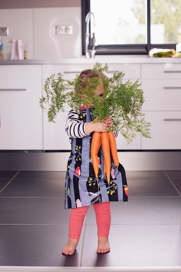 A little girl hiding behind a bunch of carrots