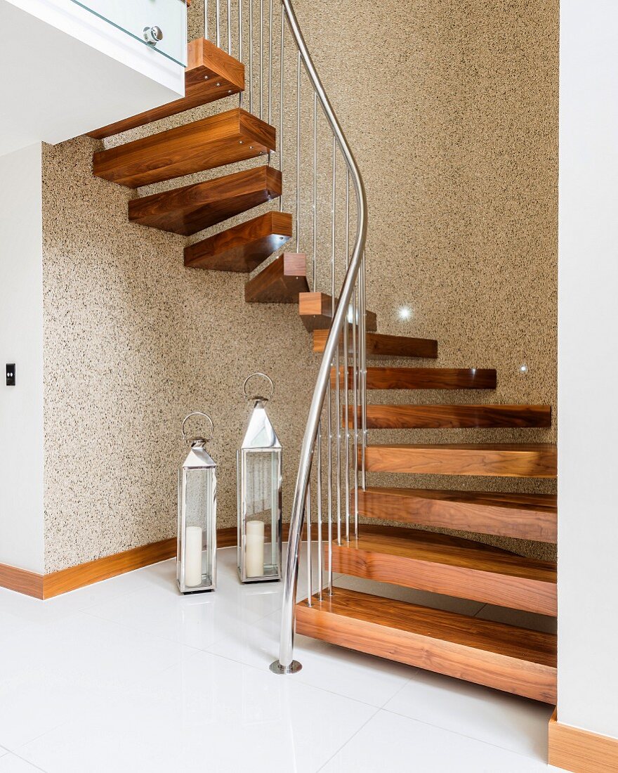 Winding staircase with wooden treads and stainless steel balustrade above lanterns on tiled floor