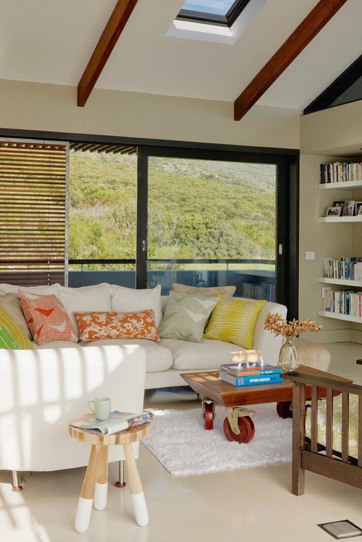 Heller Polstersofa und gemusterte Kissen vor Balkonfenster mit Ausblick, in modernem Wohnzimmer