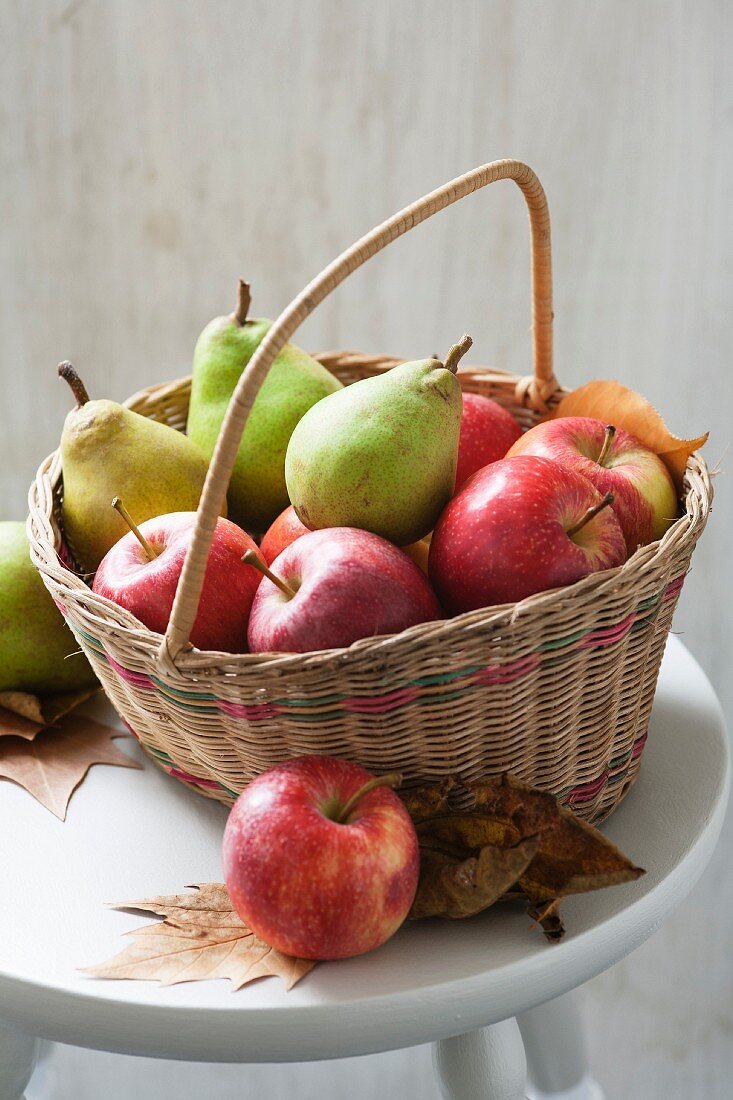 Apples and pears in a basket with autumn leaves