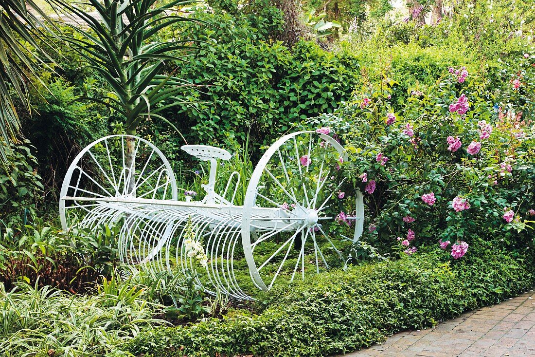 Weiß lackiertes, altes landwirschaftliches Gerät in blühendem Garten