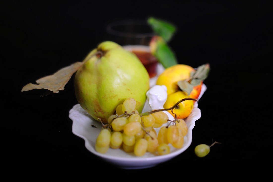 An autumnal arrangement of fruit featuring grapes, a quince and apples in a porcelain bowl