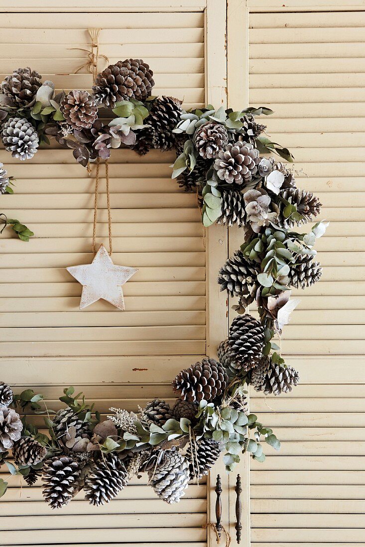 Festive wreath of pine cones with star pendant hung in vintage louvre door