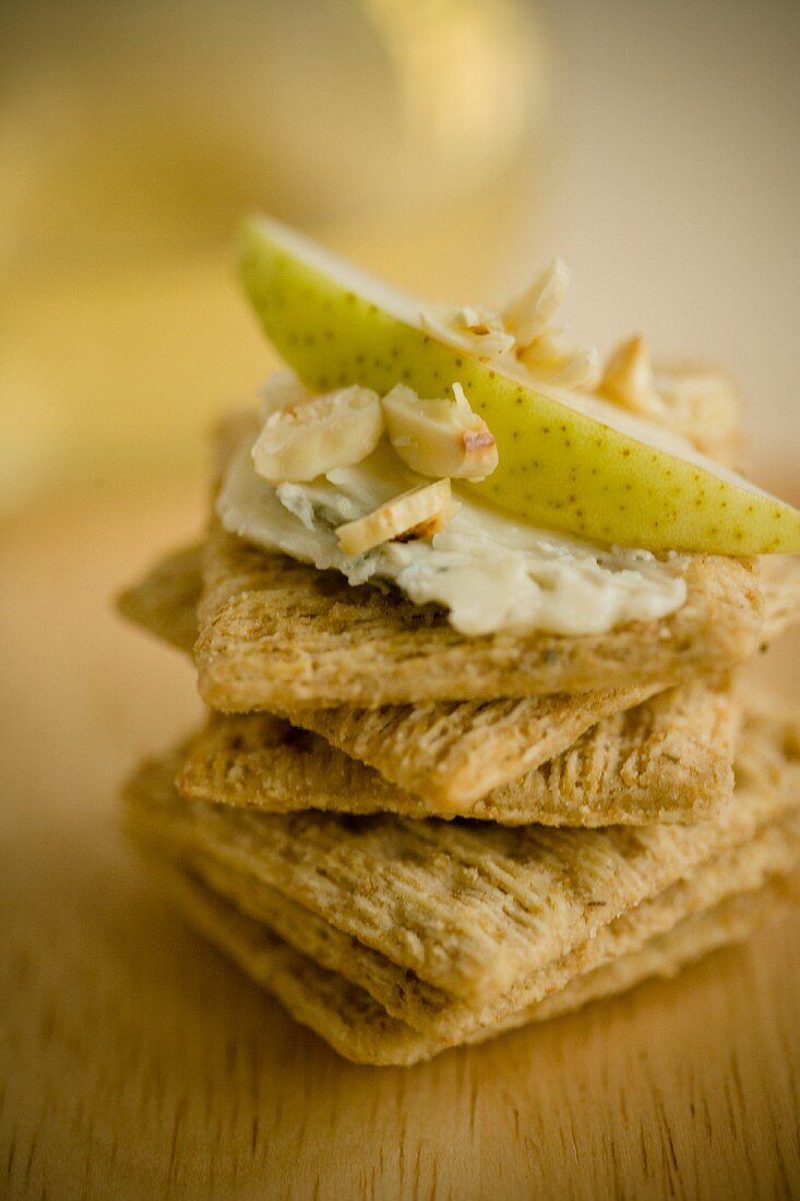 A stack of crackers topped with cheese, pear and almonds