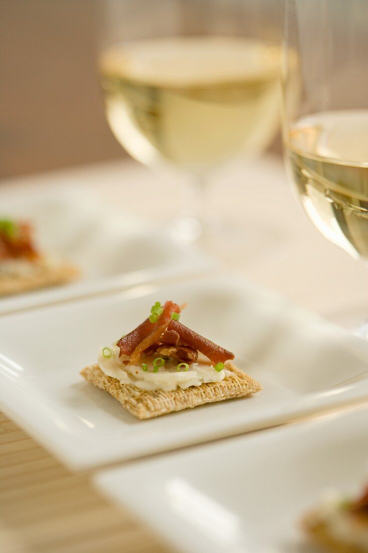 Crackers topped with cheese, bacon, salmon and chives served with white wine