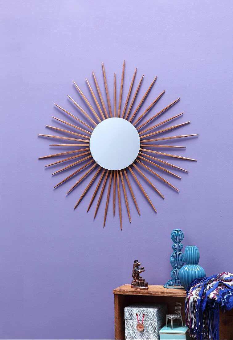 Round mirror surrounded by sunburst made from chopsticks on lilac wall