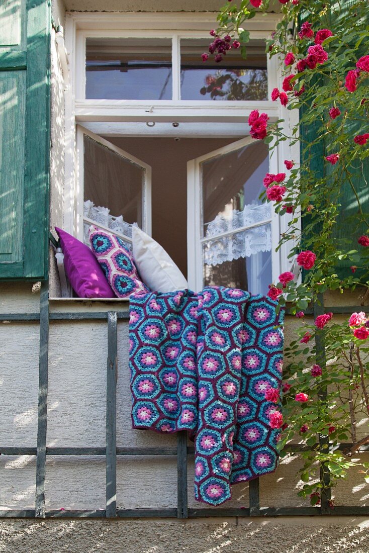 Selbstgehäkelte Tagesdecke und Kissenbezüge in 'Granny Square' auf Fensterbrett von traditionellem Sprossenfenster