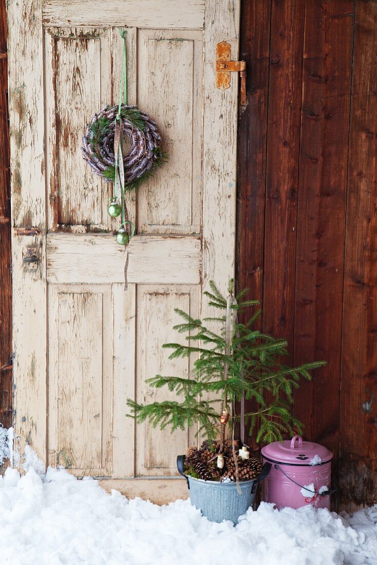 Kranz aus Zapfen und ein kleiner Tannenbaum vor einer alten Tür