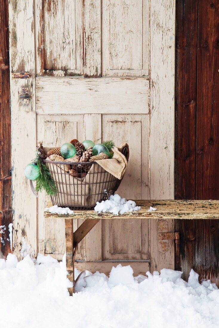Metal basket of pine cones and Christmas-tree baubles in front of old door