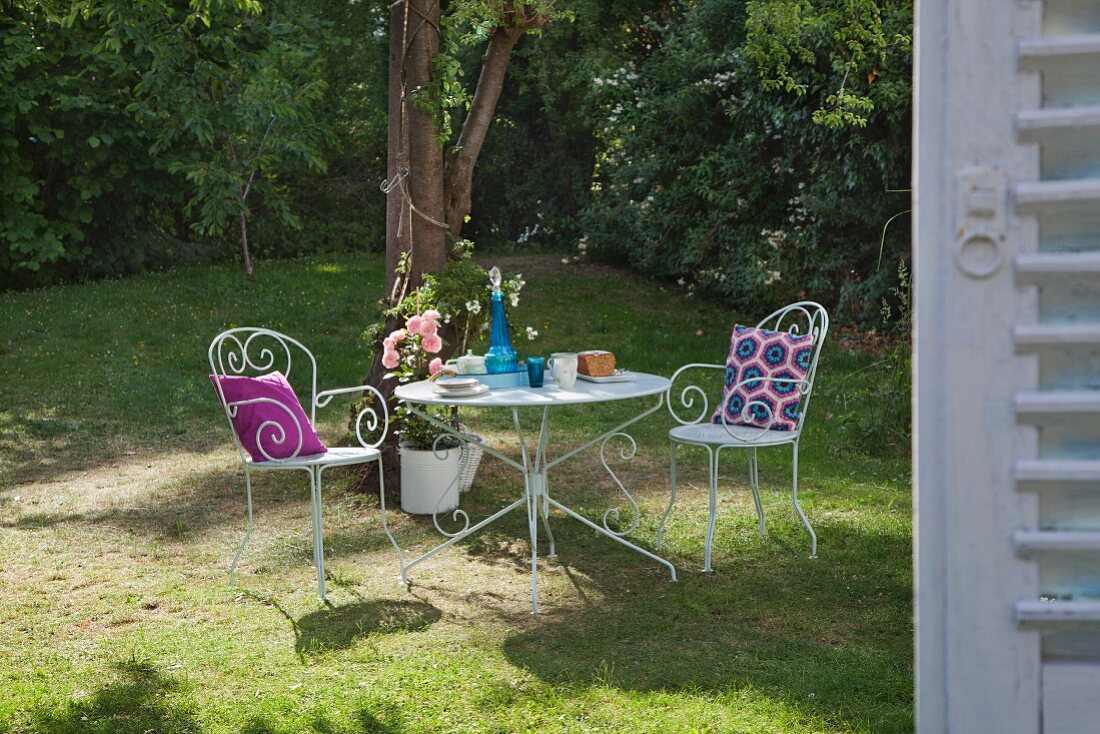 weiße Metallstühle mit Häkelkissen um gedeckten Tisch in sommerlichem Garten