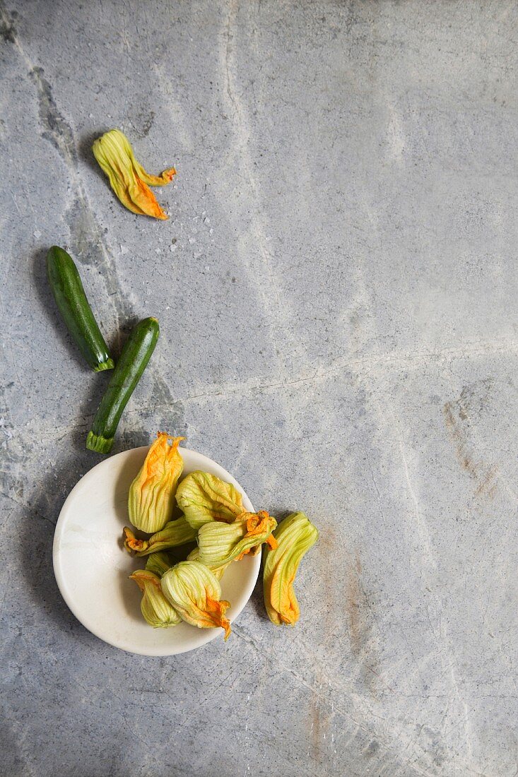 Zucchini und Zucchiniblüten auf grauem Steinuntergrund