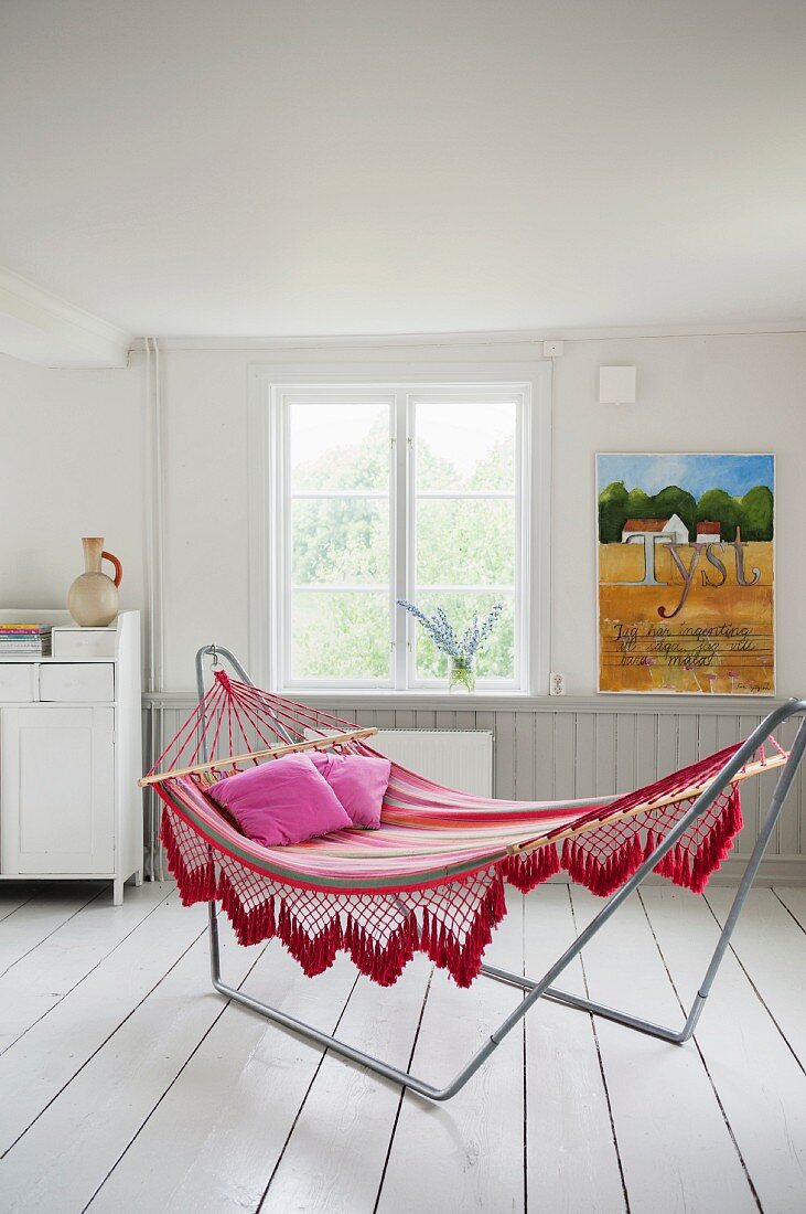 Comfortable hammock on metal frame on white wooden floor in rustic interior