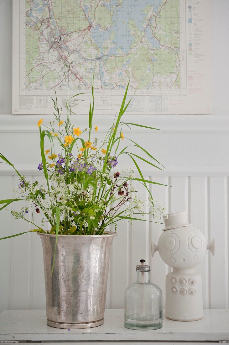 Silver vase of wildflowers, oil lamp and ornament in front of map of Sweden