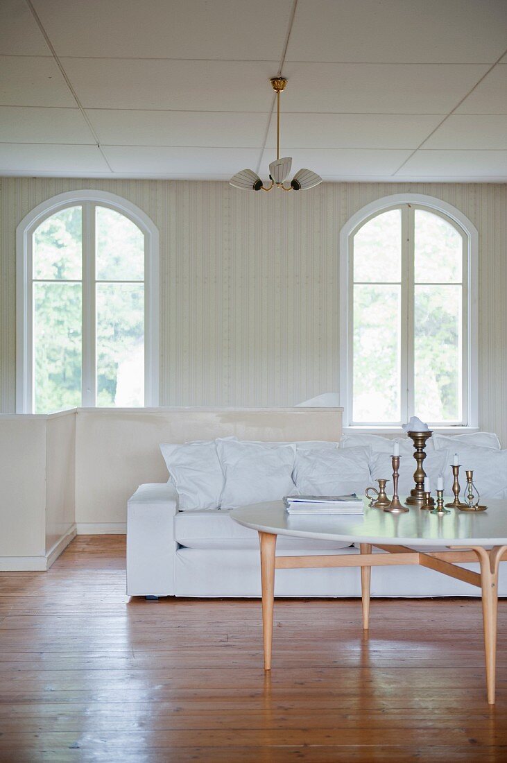 Round coffee table in front of white sofa and arched windows