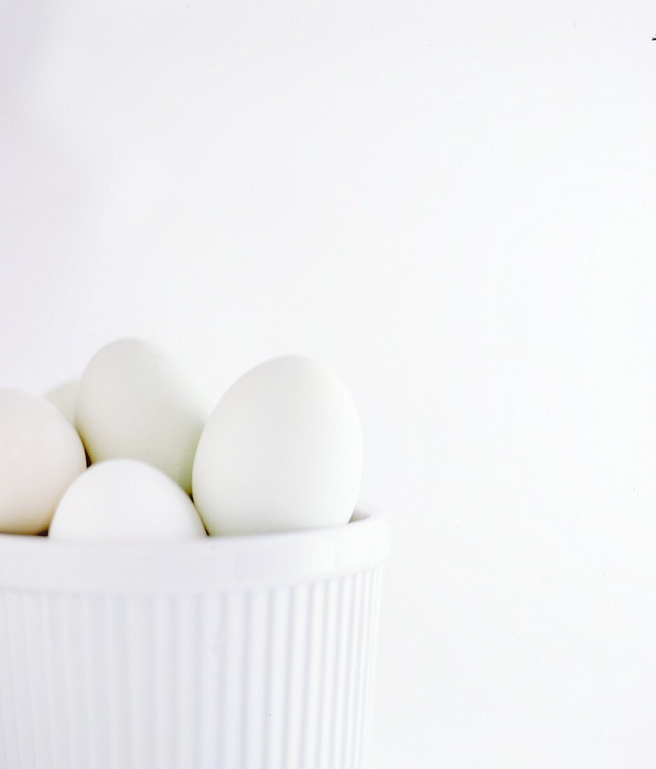 White hens eggs in a white bowl on a white surface