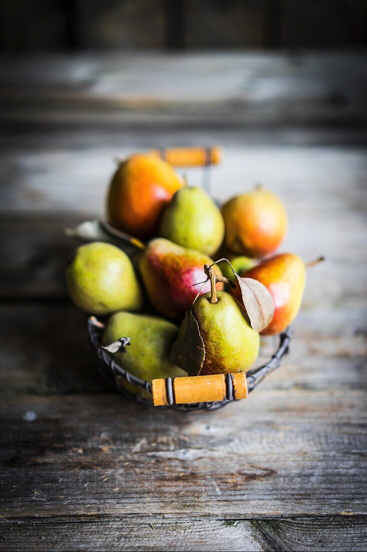 Autumn pears in a wire basket on a rustic wooden surface